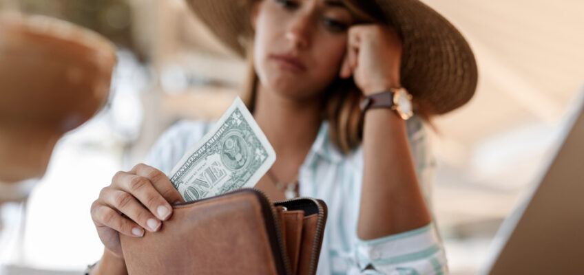 Close-up of a woman having a single dollar bill in her wallet, her expression conveying financial worry for Canada eTA application.