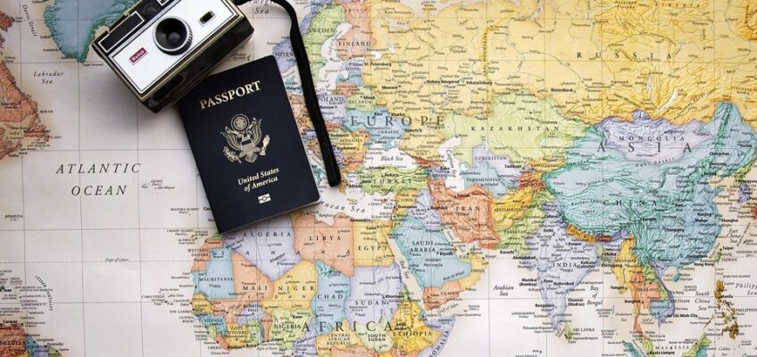 A world map with a US passport and a vintage camera placed on top, symbolizing international travel and the requirements needed for entry into different countries.