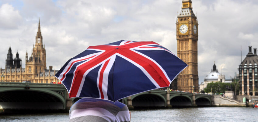 A young man's back with umbrella (UK flag design) as he observes the River Thames.