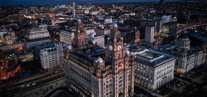 Aerial night view of Liverpool cityscape, highlighting iconic buildings with street lights and city glow.