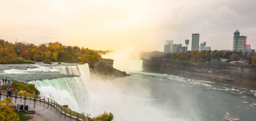 Niagara Falls with a misty backdrop, overlooked by autumn-colored trees and a city skyline, symbolizing Canadian tourist attractions for Filipinos with new visa-free travel policy.