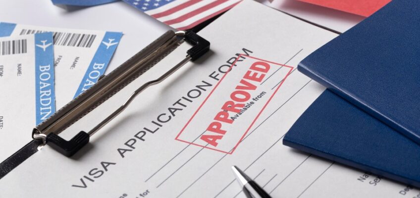 An image of a clipboard with a visa application form marked "APPROVED" under a paperclip, surrounded by various national flags, and boarding passes, representing a successful K-1 fiancé visa application.