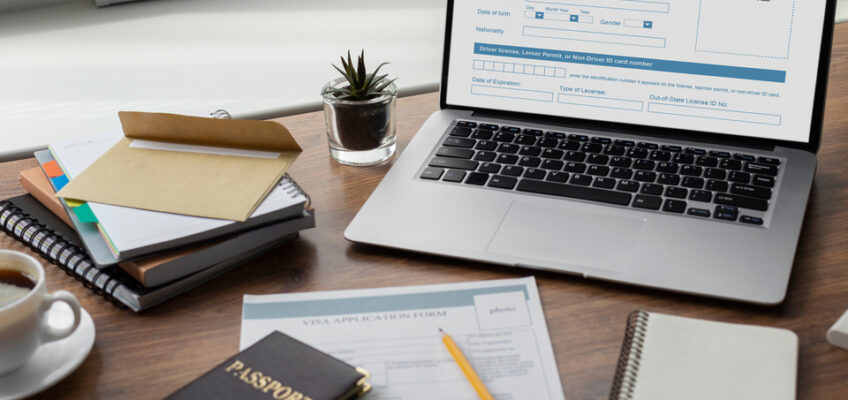 A laptop displaying a 'Photo Here' placeholder for ID application, with a passport and visa application form on a desk, indicative of the process of applying for travel documents.