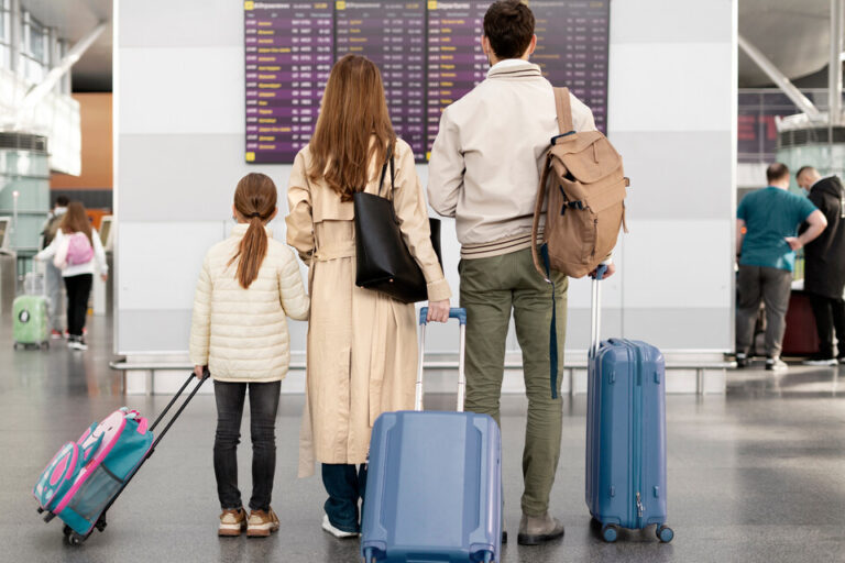 A family of three with suitcases looks at a flight information display in an airport, ready for travel.